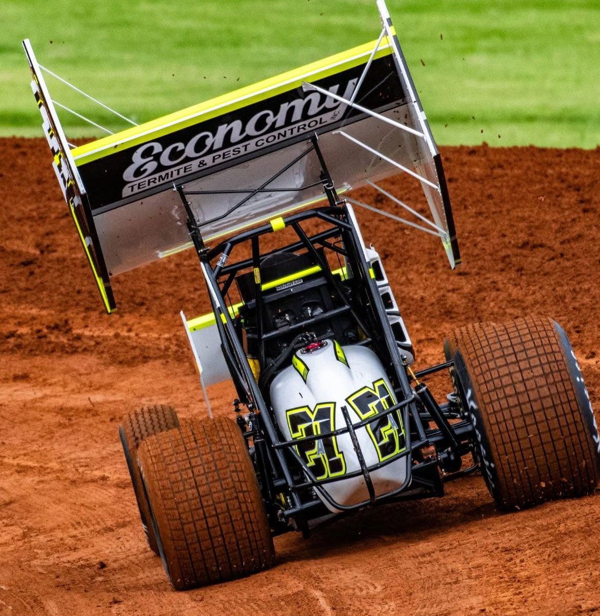 Sprint car racing on a dirt track, with a black and white car sliding through a turn