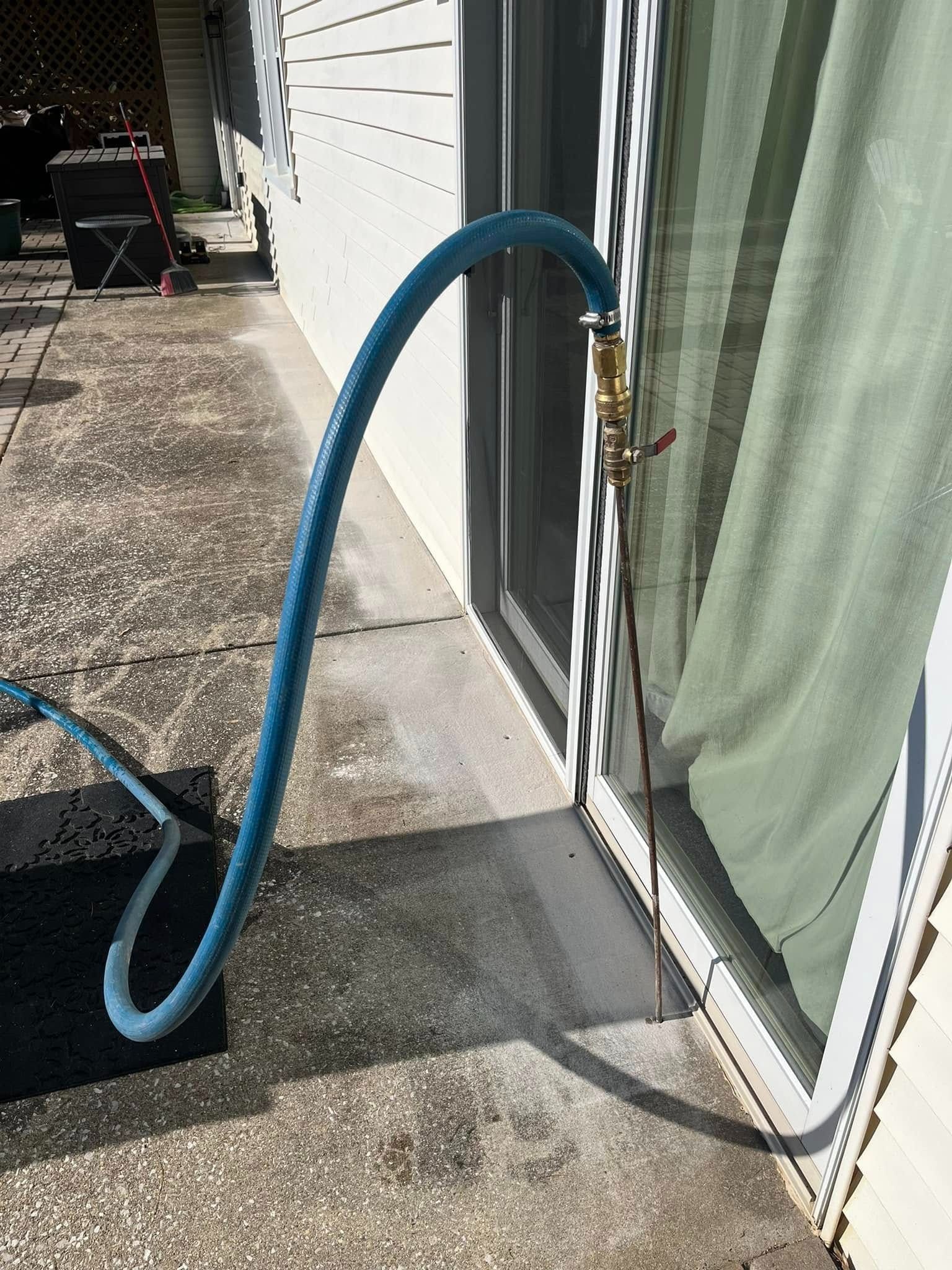 Blue hose connected to an outdoor faucet beside a sliding glass door and curtain