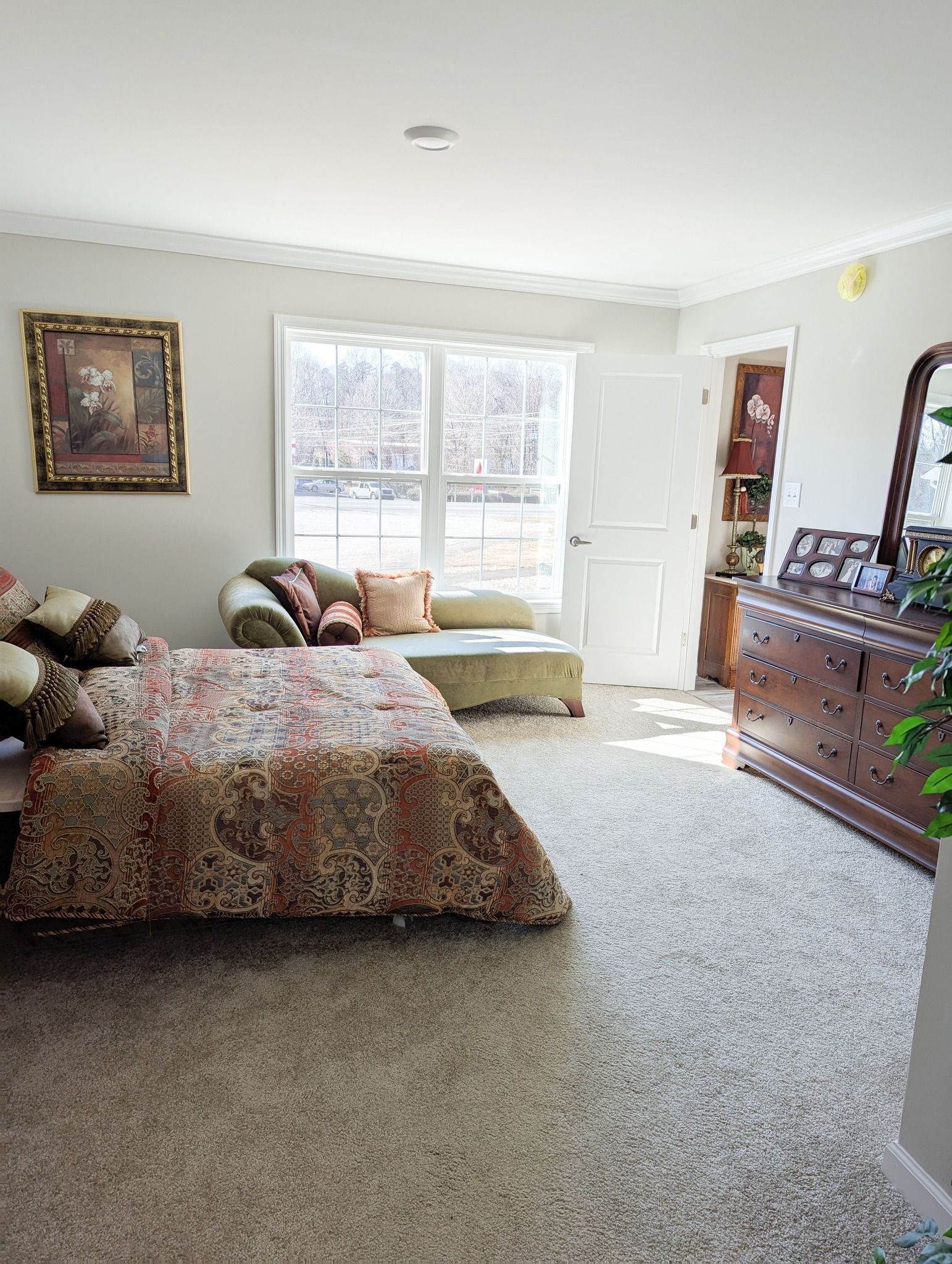 A bedroom with a bed, dresser, chair and mirror.