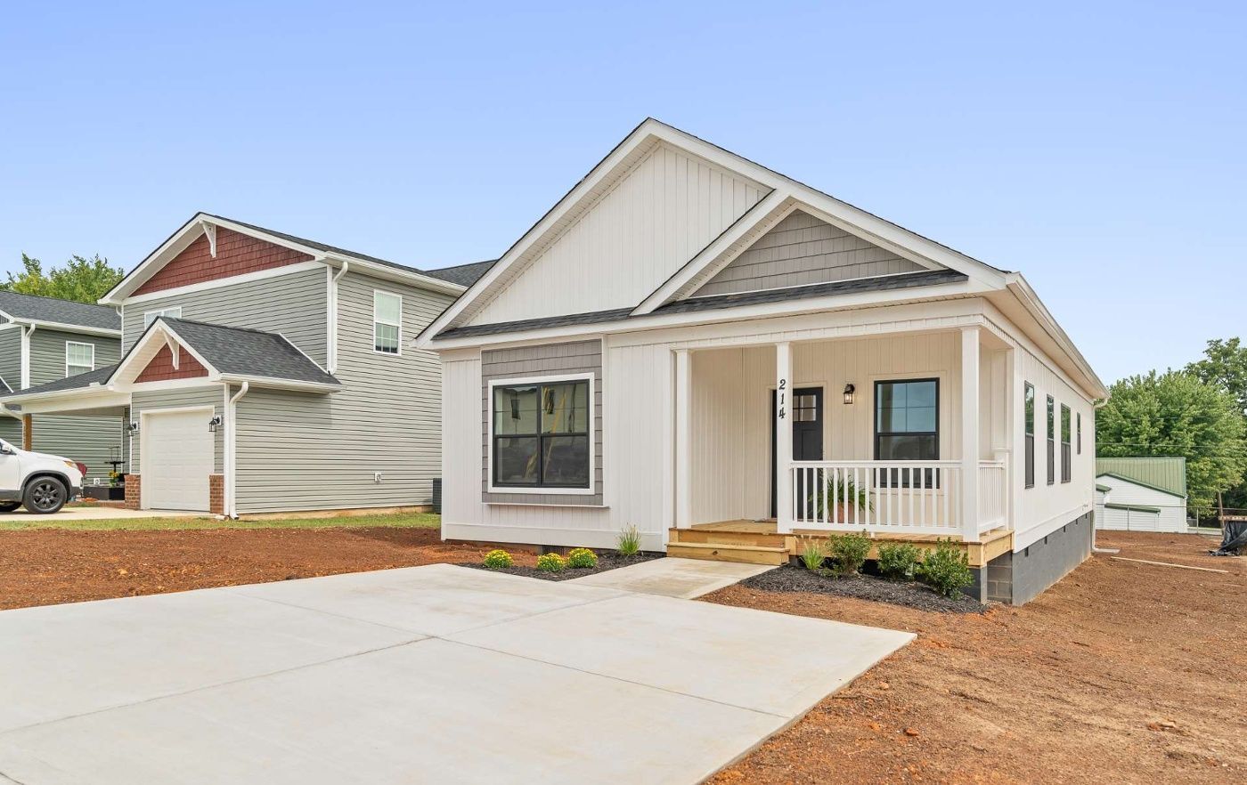 A white house with a porch and a car parked in front of it.