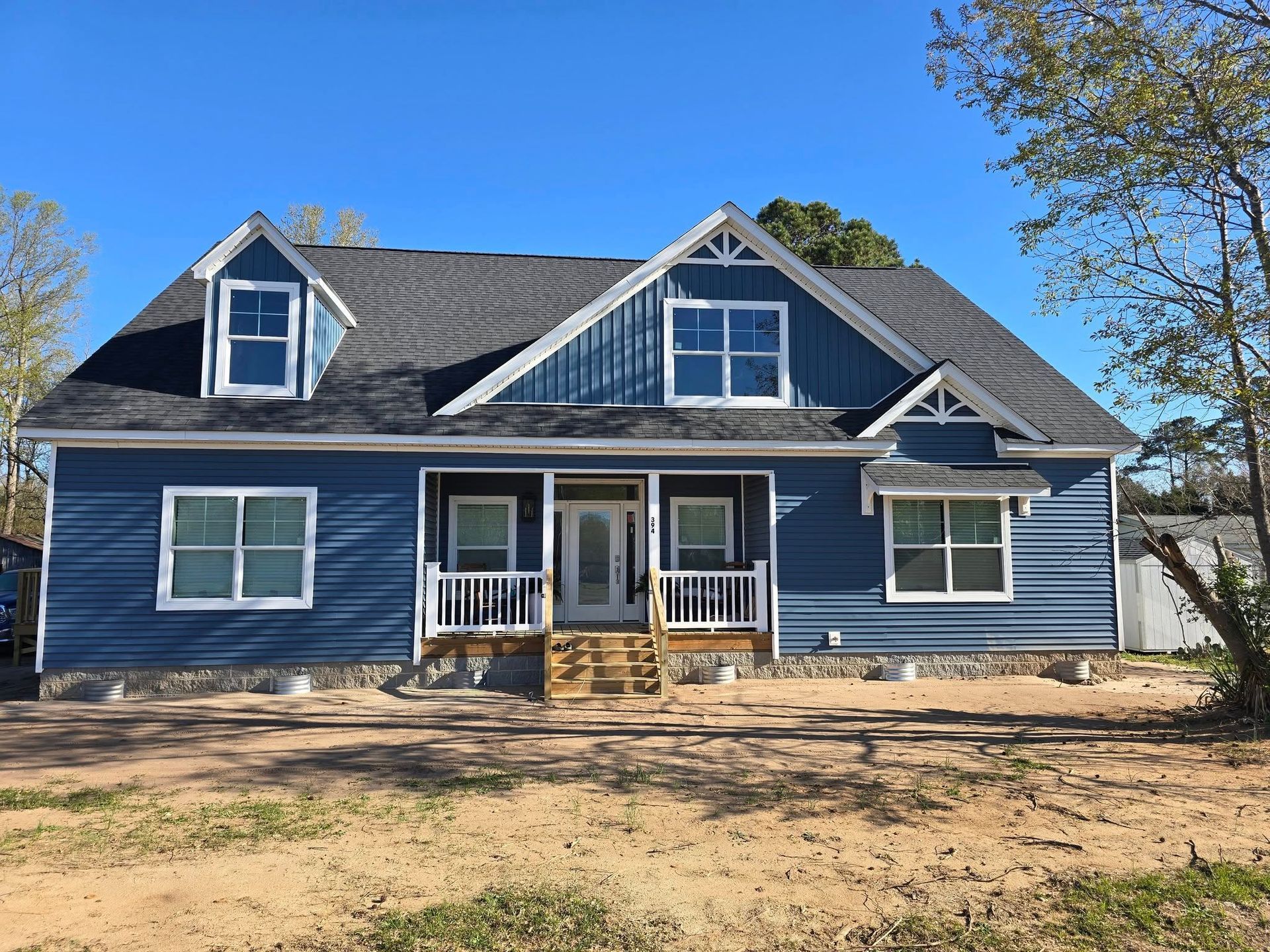 A white house with a gray roof and a porch surrounded by trees.