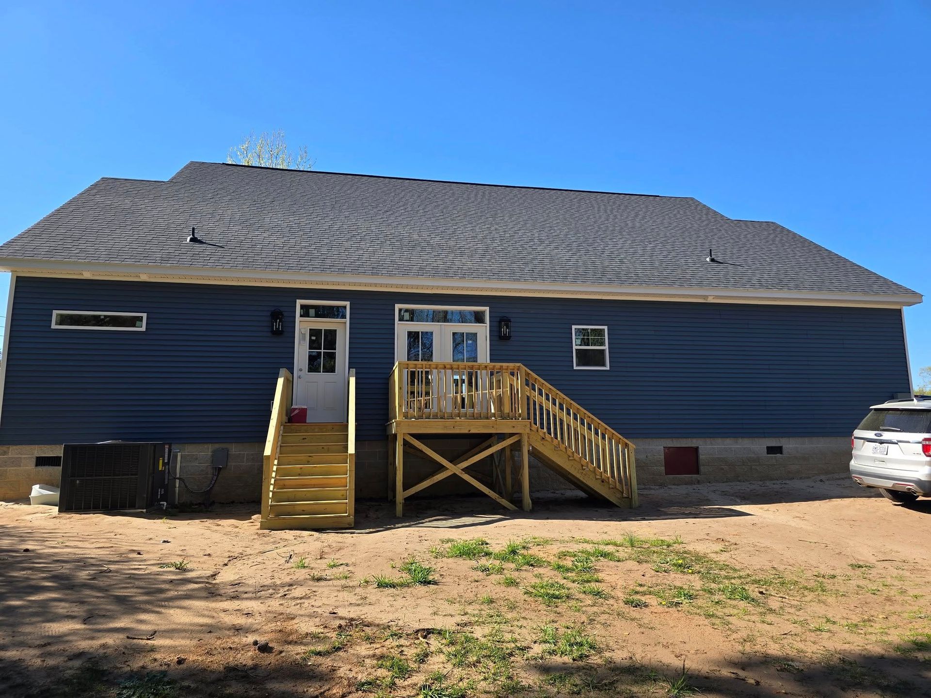 The back of a blue house with a wooden deck and stairs.