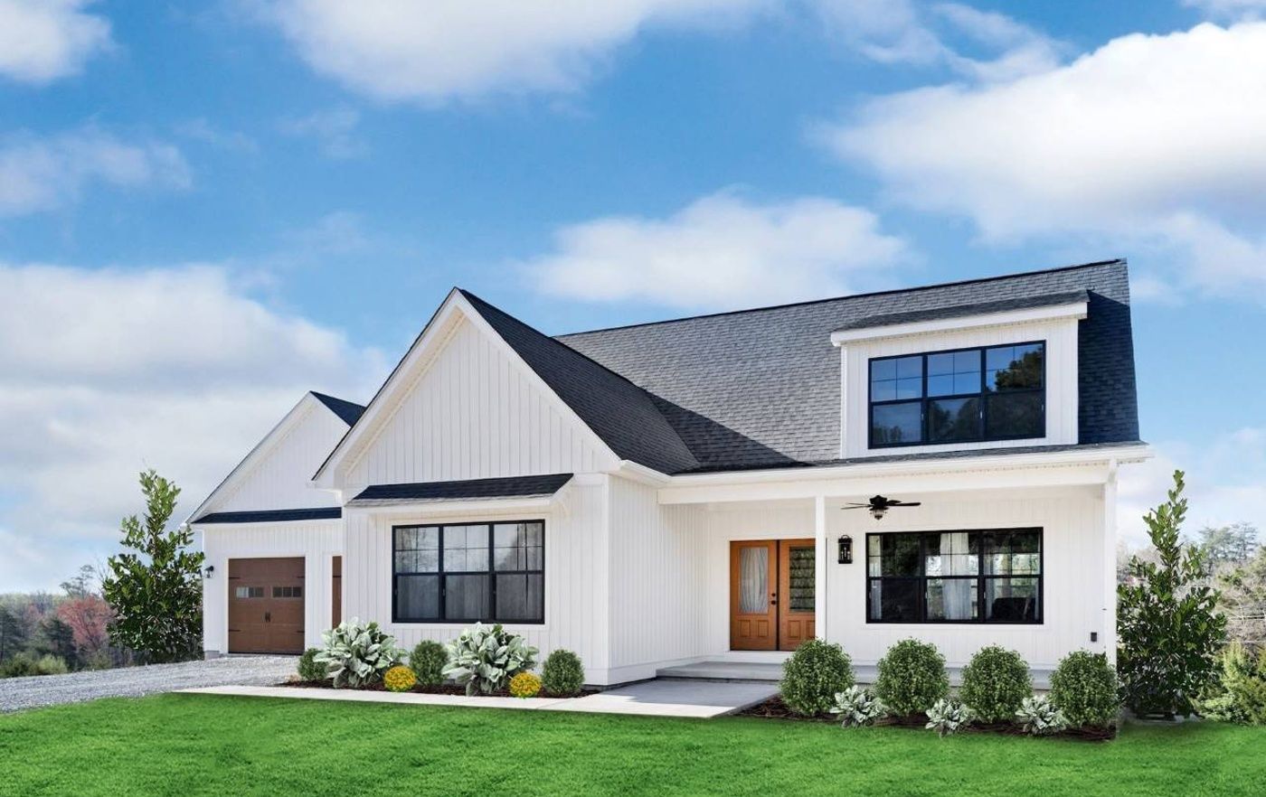 A white house with a black roof is sitting on top of a lush green lawn.