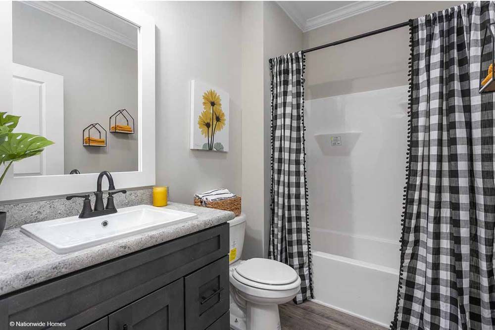 A bathroom with a sink, toilet, shower and black and white checkered curtains.