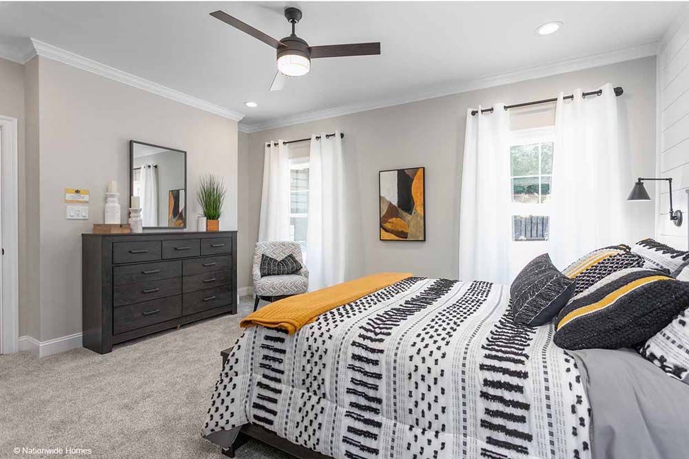 A bedroom with a bed, dresser, mirror and ceiling fan.