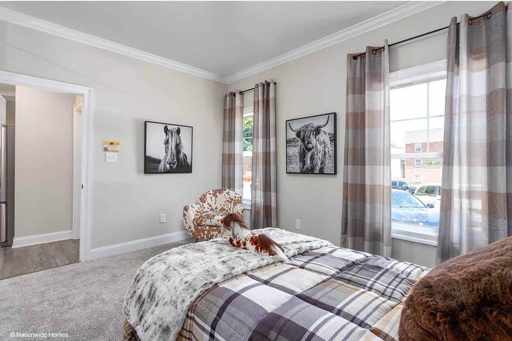 A bedroom with a bed, chair, window and paintings on the wall.