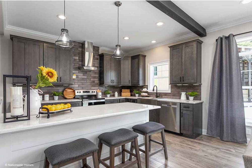 A kitchen with gray cabinets, white counter tops, stainless steel appliances and a large island.