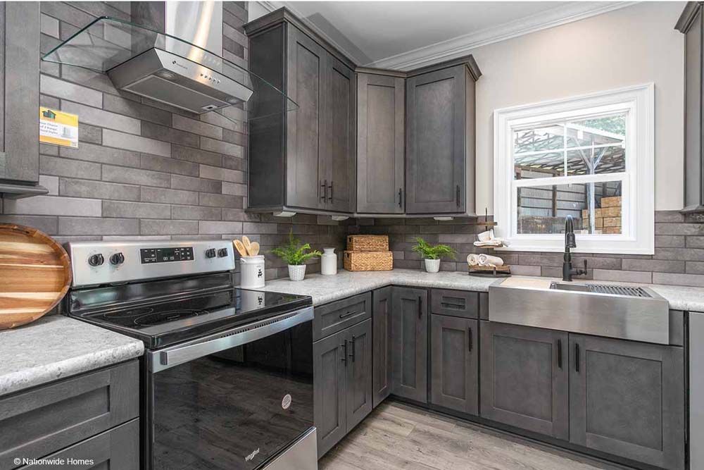A kitchen with gray cabinets, a stove, a sink, and a window.