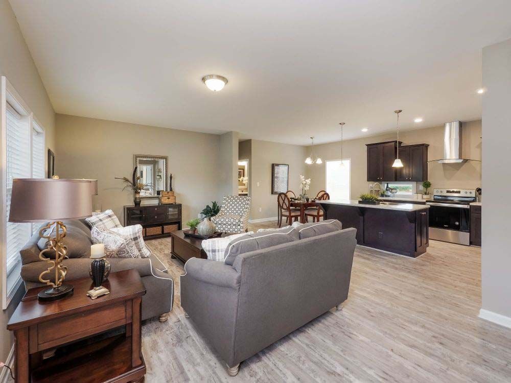 A living room with a couch, table, lamp and a kitchen.