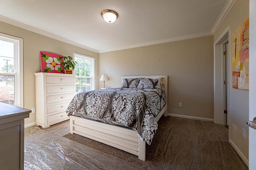 A bedroom with a bed, dresser, and two windows.