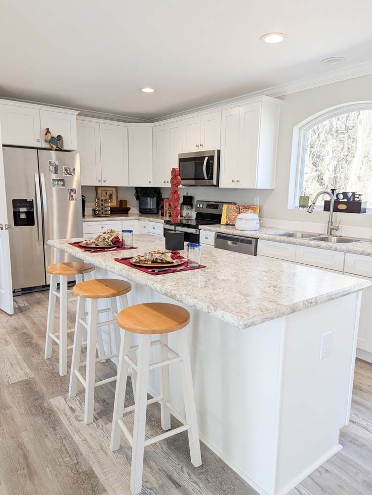 A kitchen with white cabinets, granite counter tops, stools and a large island.