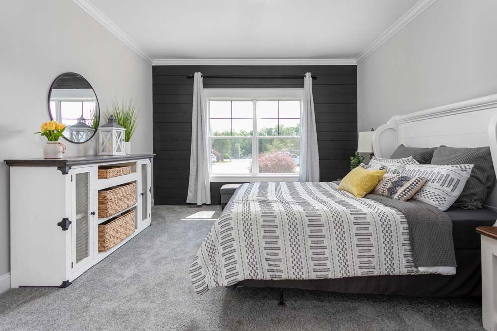 A bedroom with a bed, dresser, mirror and window.