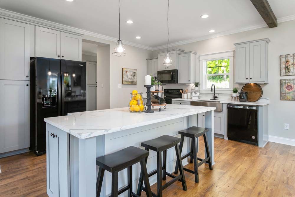 A kitchen with a large island, stools, a refrigerator and a dishwasher.
