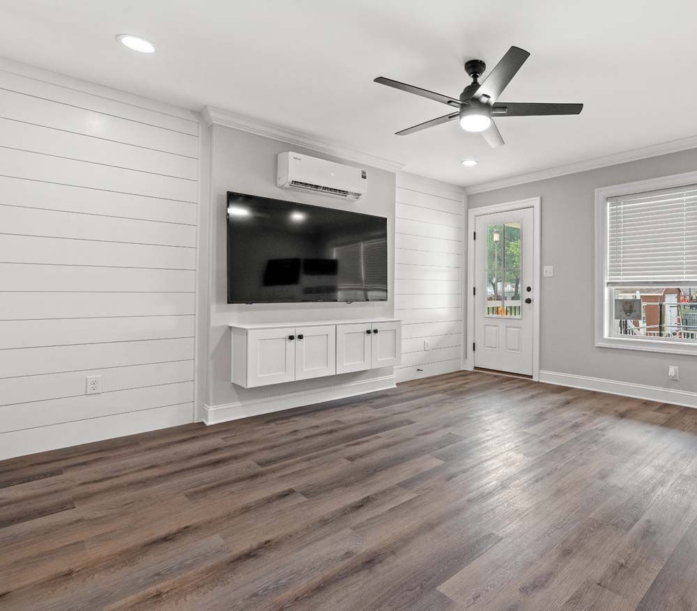 A living room with a flat screen tv mounted on the wall and a ceiling fan.