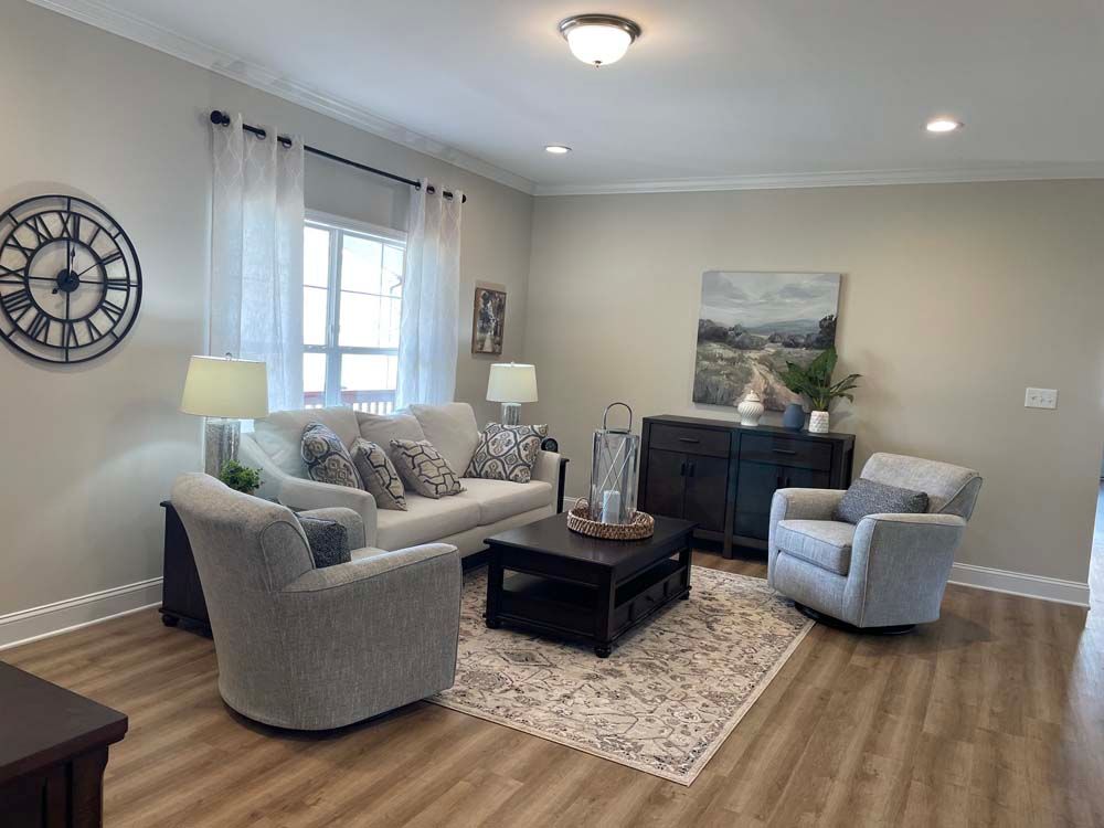 A living room with a couch, two chairs, a coffee table and a clock on the wall.