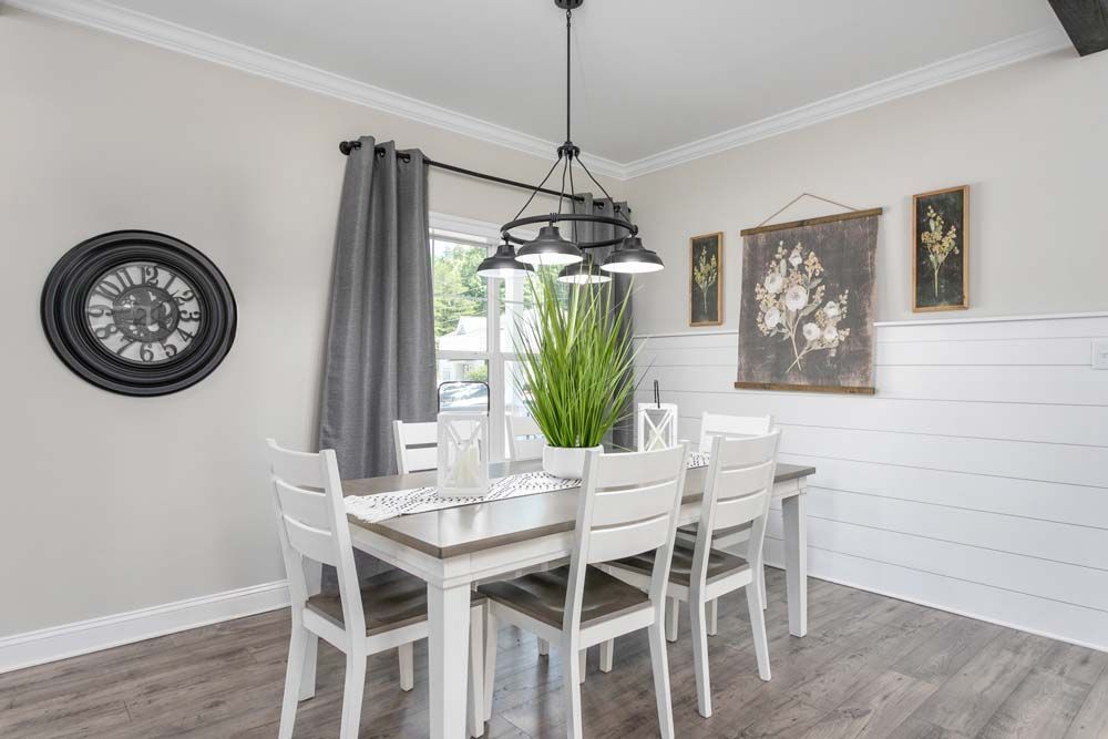 A dining room with a table and chairs and a clock on the wall.
