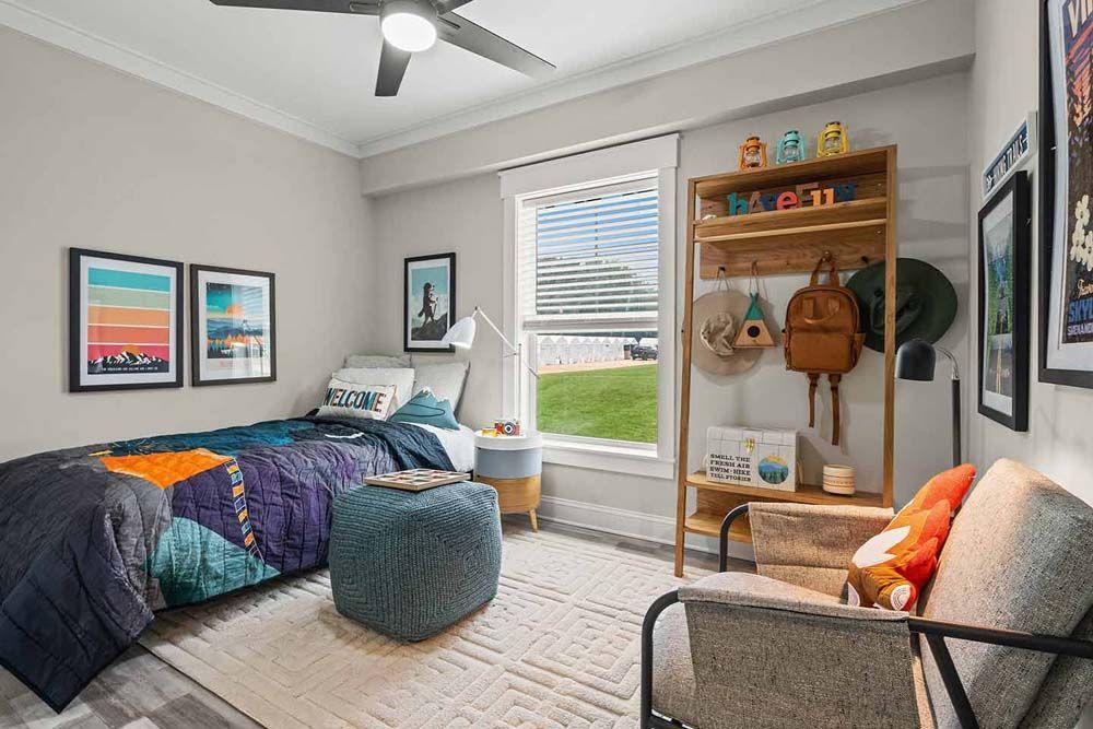 A bedroom with a bed, chair, and ottoman and ceiling fan.