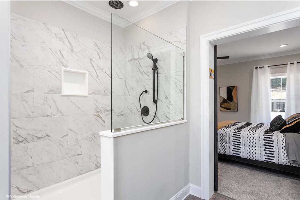 A bathroom with a walk in shower and a bed in the background.