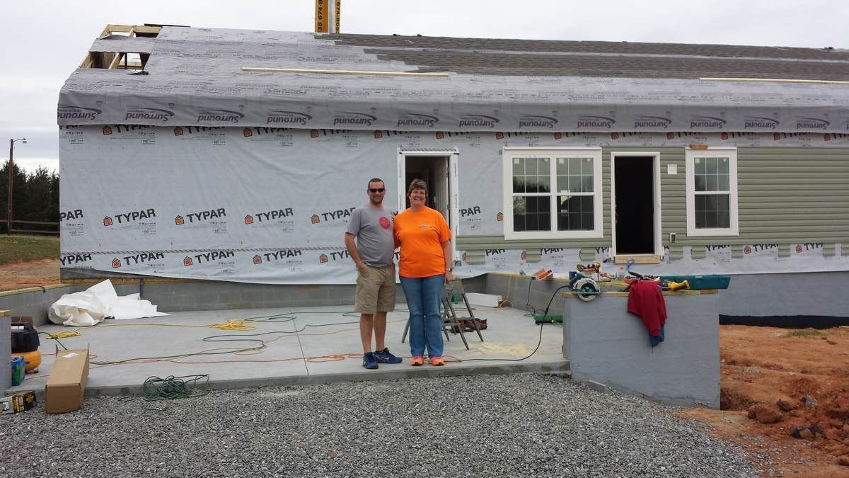 A man and a woman are standing in front of a house under construction.