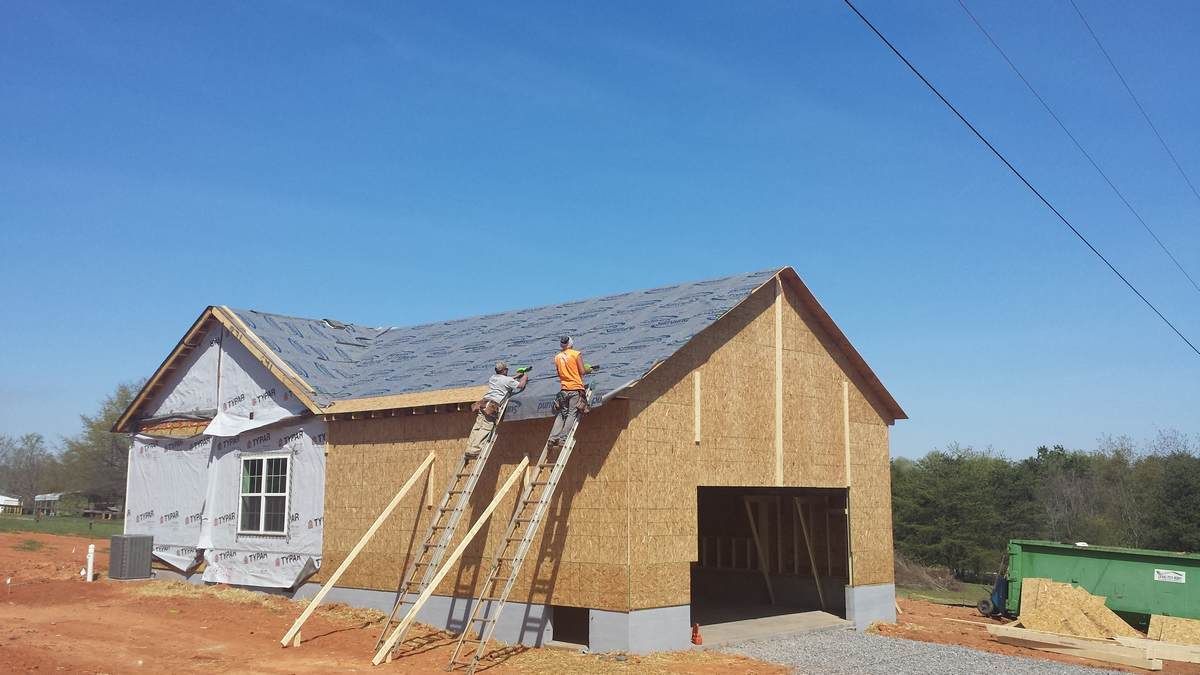 A man on a ladder is working on the roof of a house under construction.