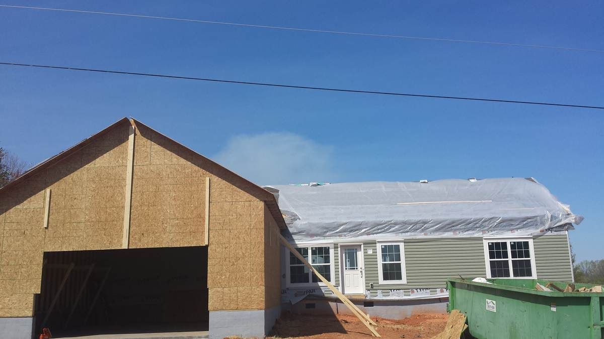 A house under construction with a green dumpster in front of it.