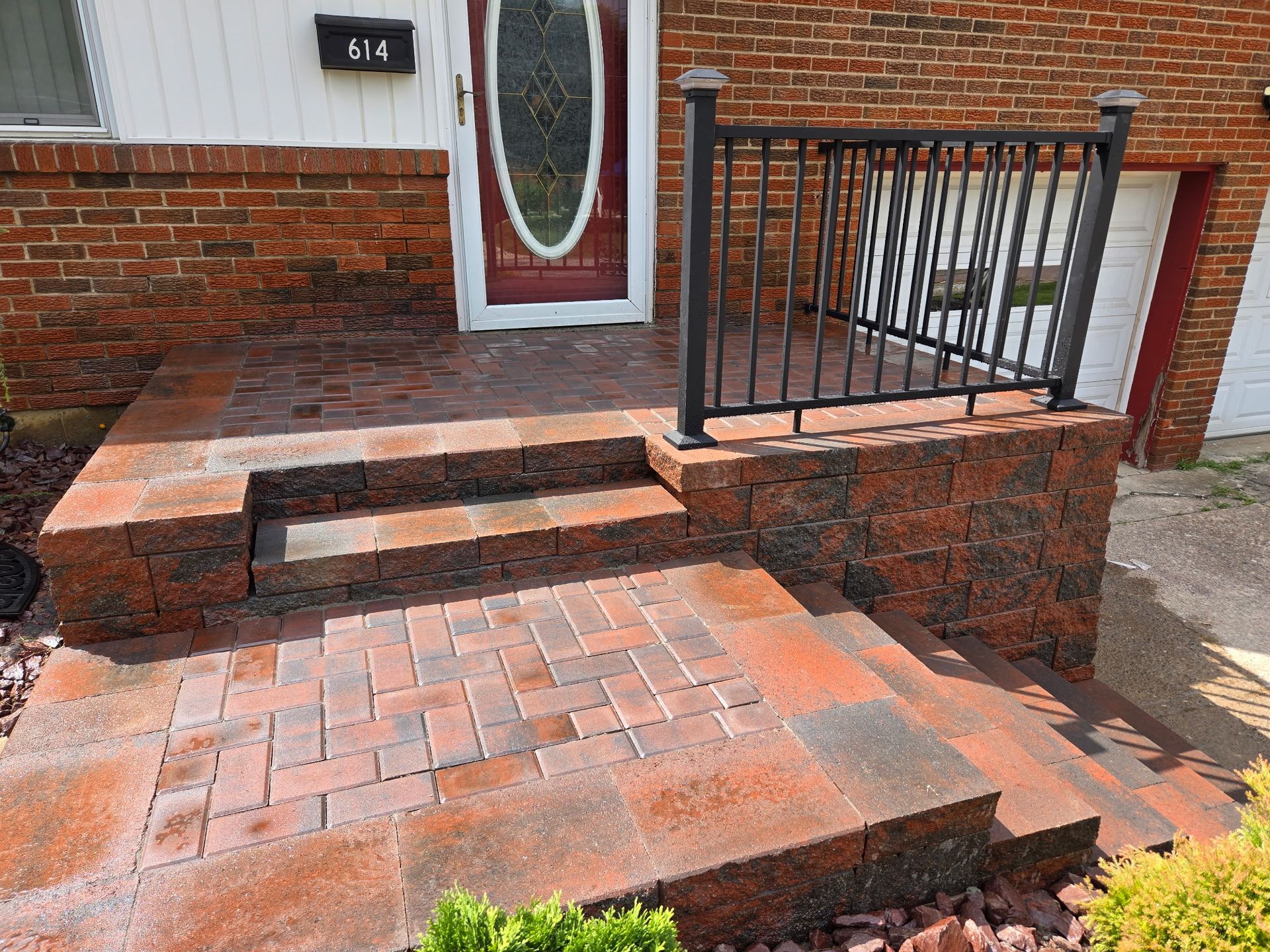 Front steps and brick ramp leading to a house entrance with black railing and red door