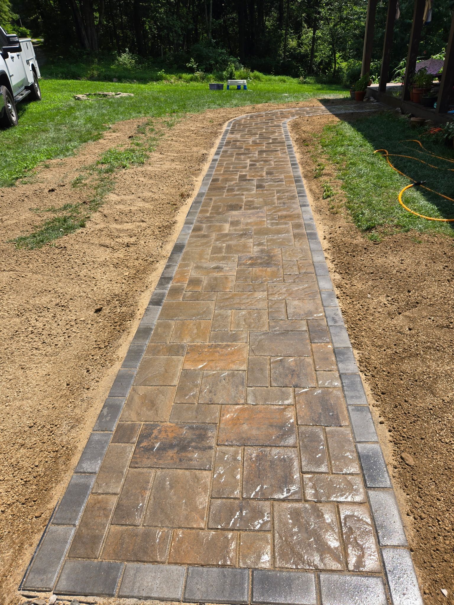 Brick walkway under construction, bordered by dirt and grass in a sunny yard
