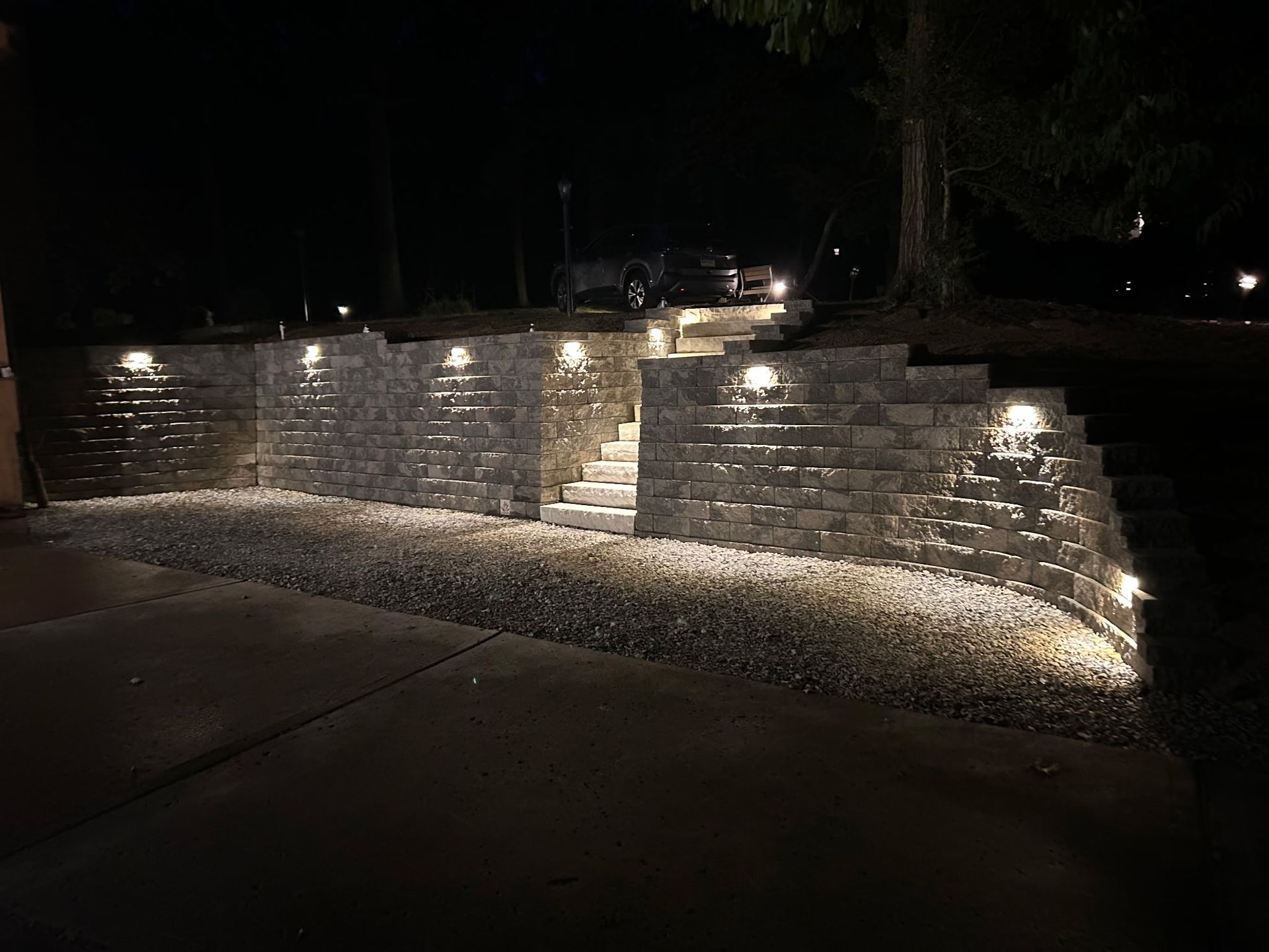 Lit stone retaining wall with steps and pathway lights at night