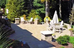 A patio with a table and chairs and an umbrella in a backyard.