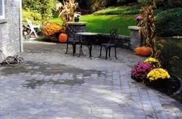 A patio with a table and chairs surrounded by pumpkins and flowers.