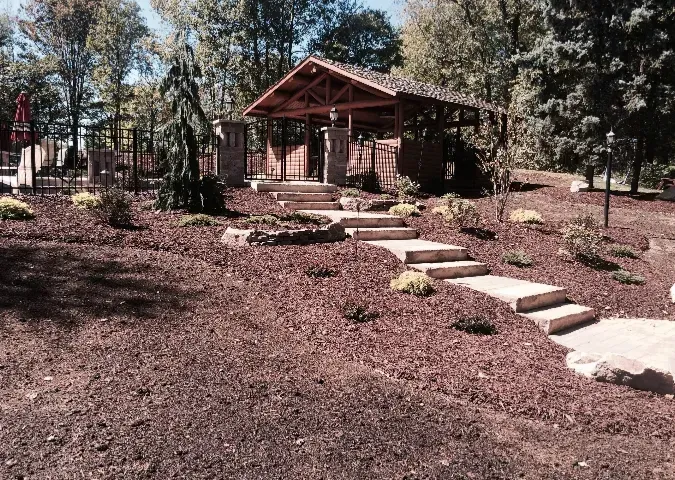 Trees and mulch surround a house with stairs leading up to it.