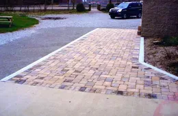 A car is parked in a driveway next to a brick walkway.