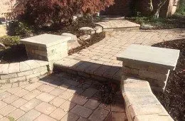 A brick walkway with steps and a stone wall in a garden.