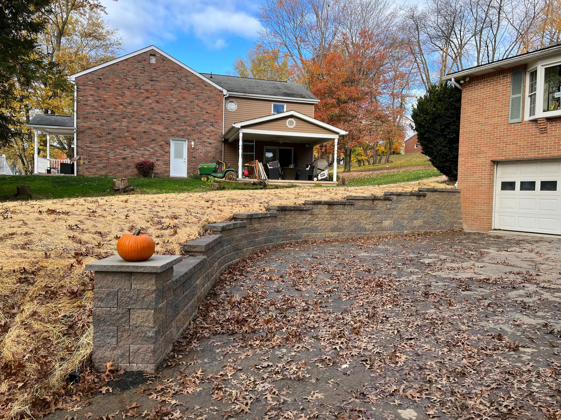 A pumpkin is sitting on a brick wall in front of a house.