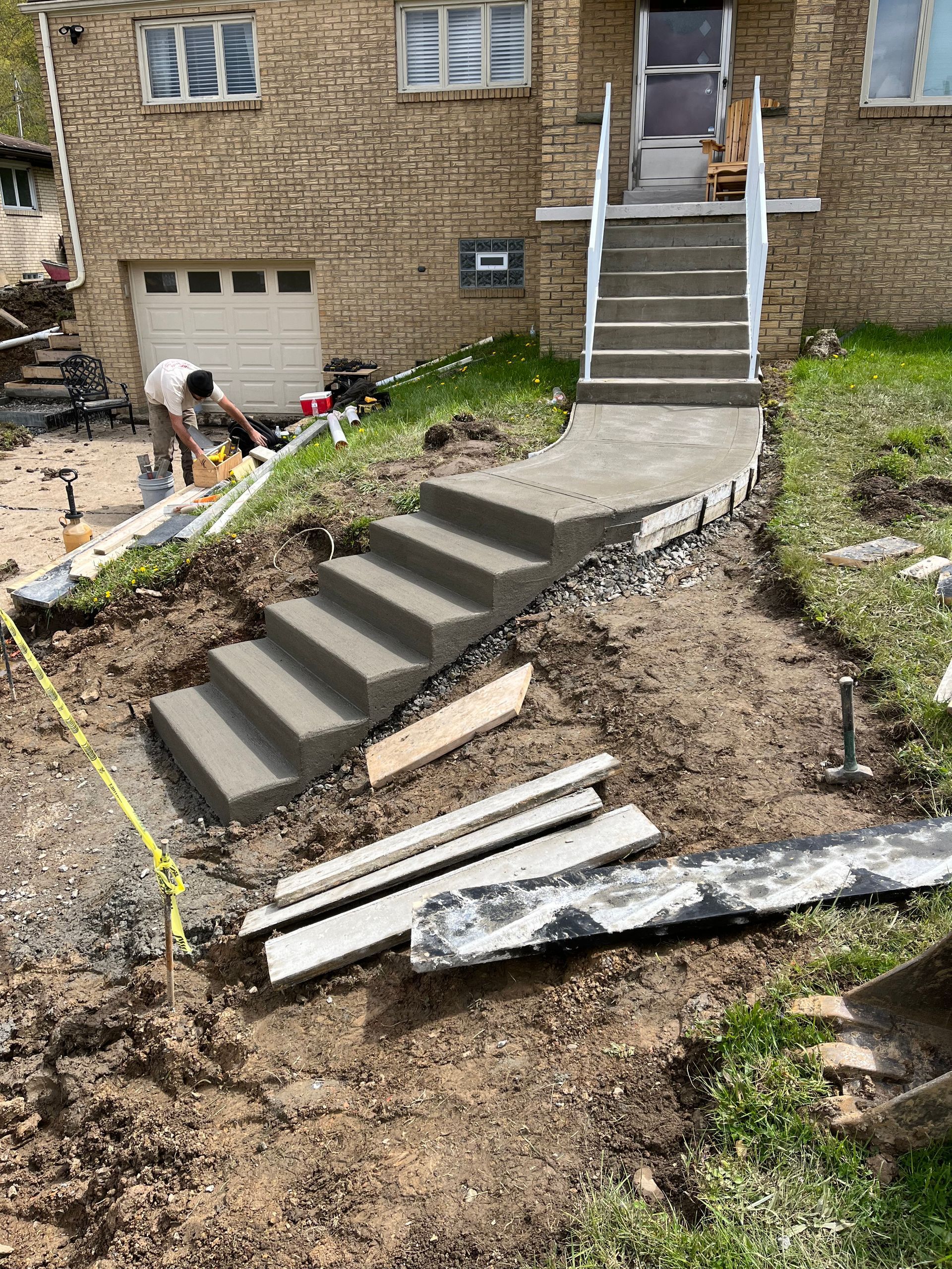 A man is laying concrete steps in front of a brick house.