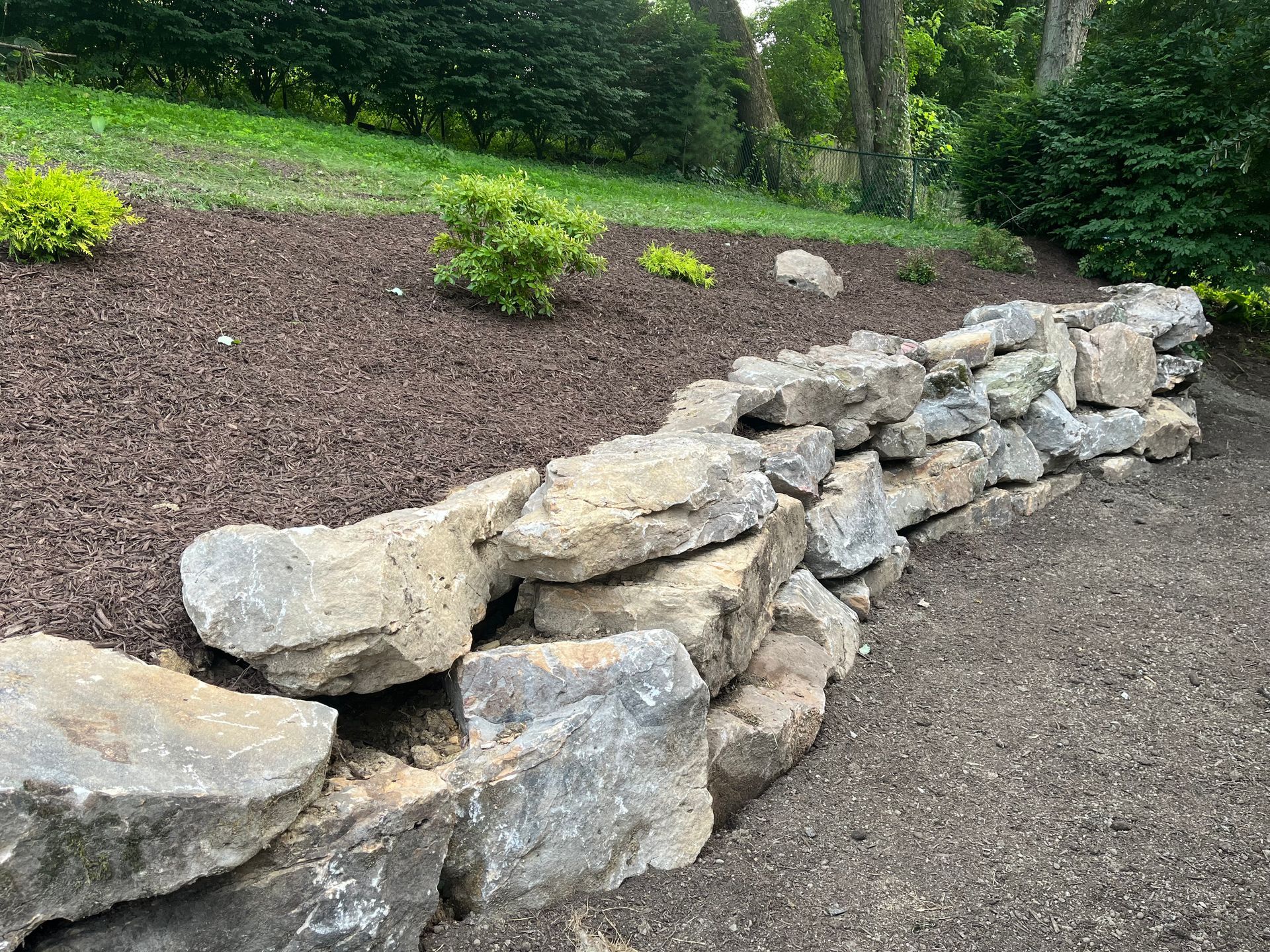 A rock wall in a garden with trees in the background.