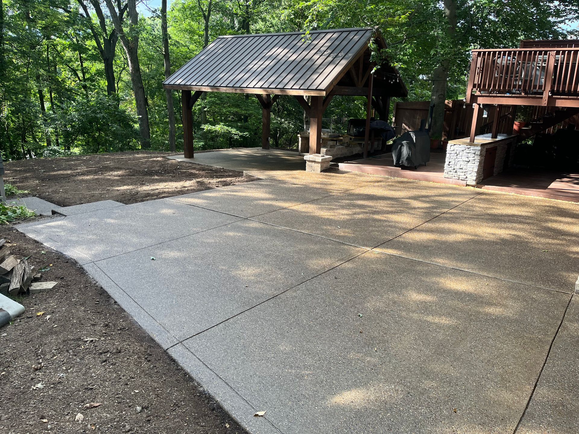 A concrete driveway with a gazebo and a deck in the background.