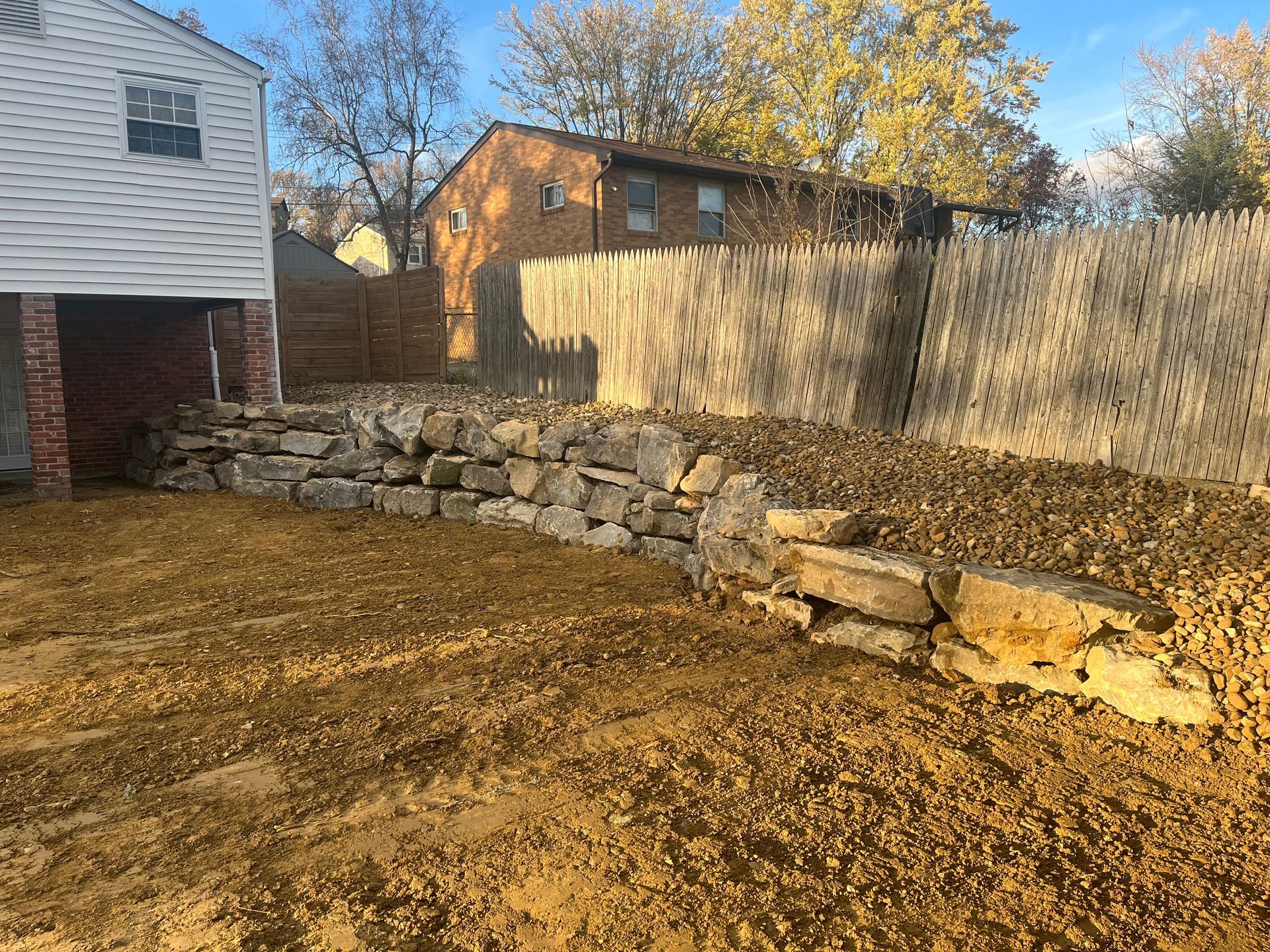 A stone wall is being built in the backyard of a house.