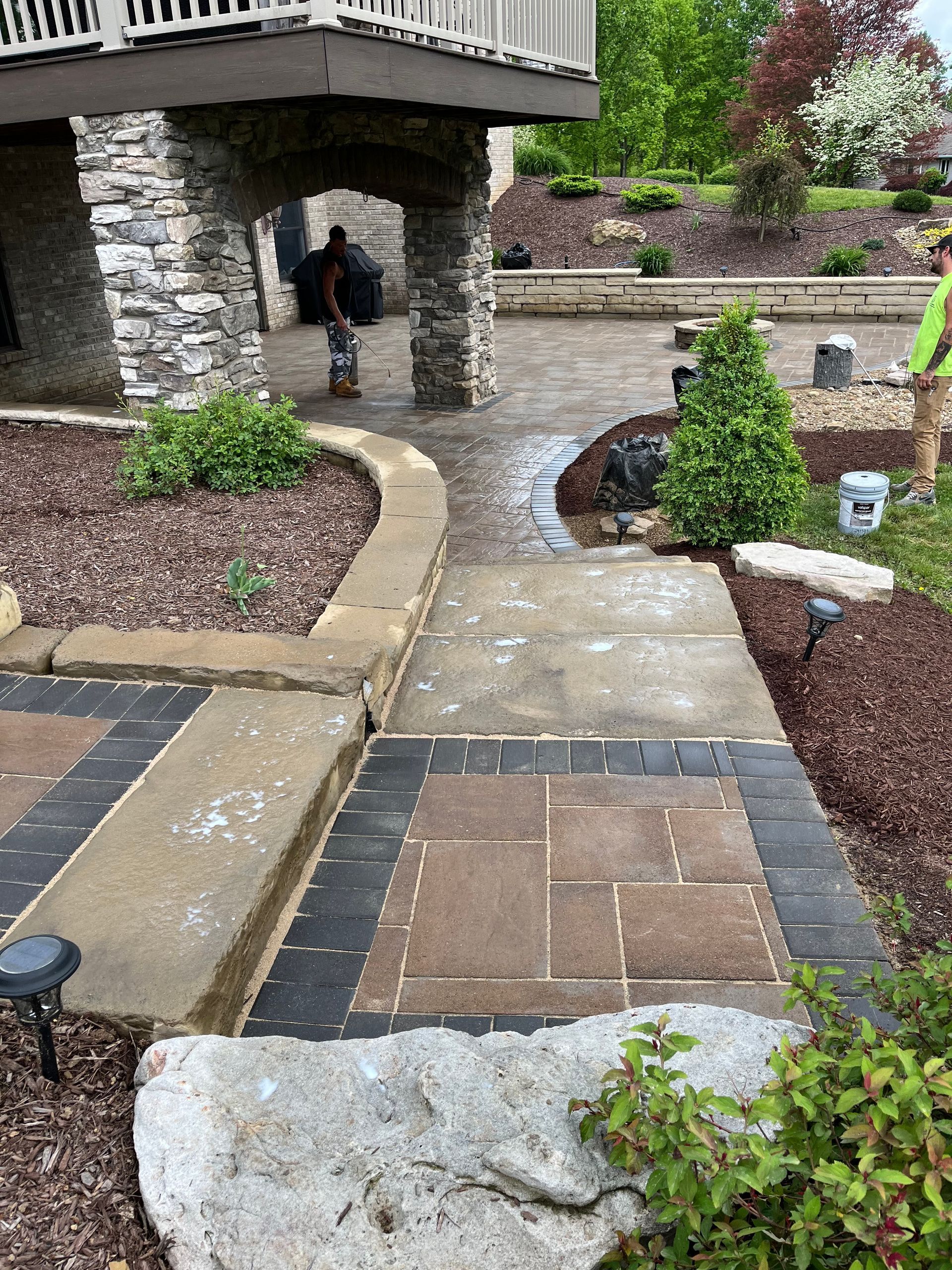 A brick walkway leading to a deck in a backyard.