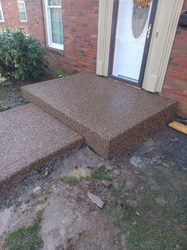 A concrete walkway is being built in front of a brick house.