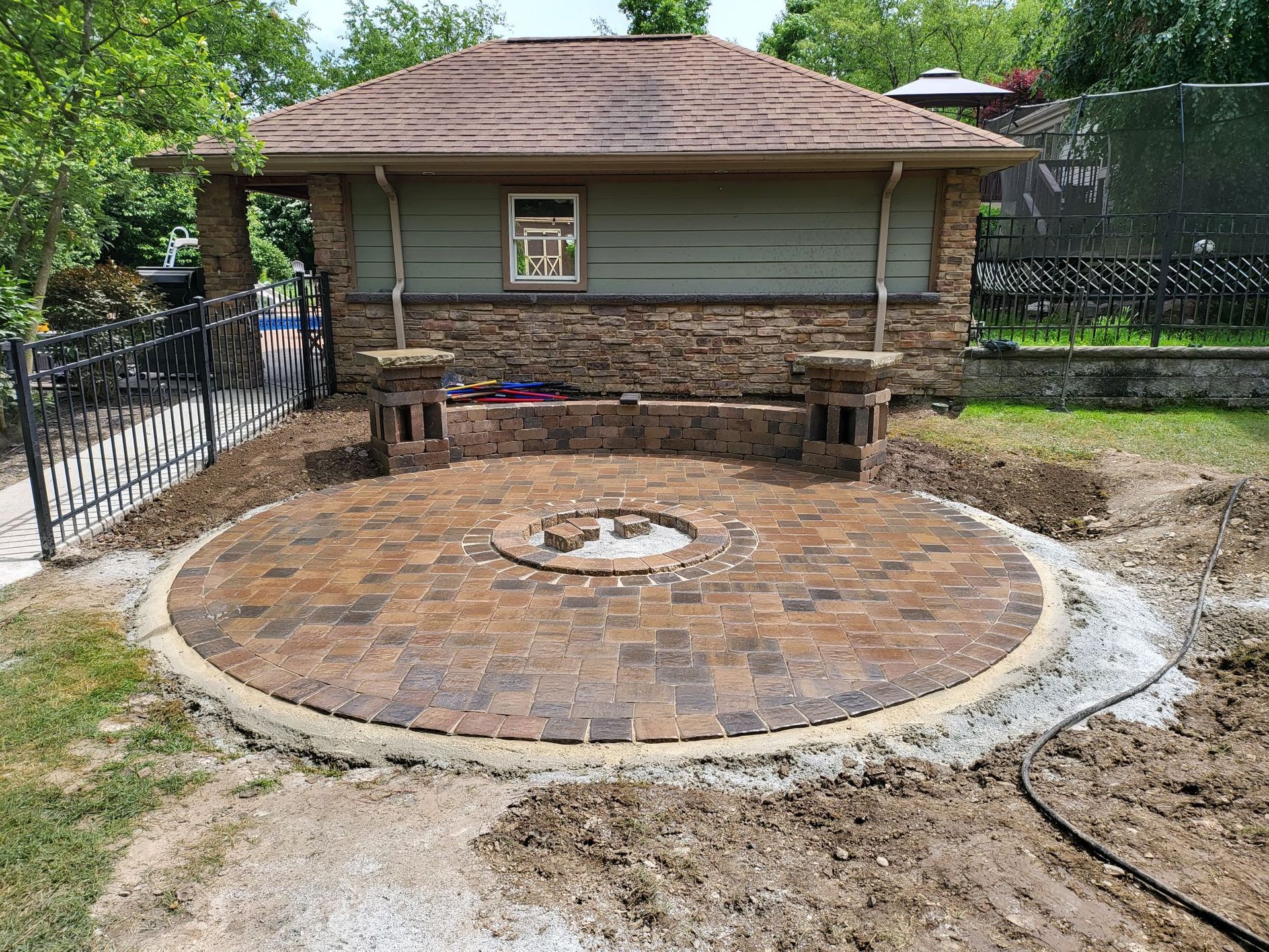 A brick patio with a fire pit in the middle of it in front of a house.