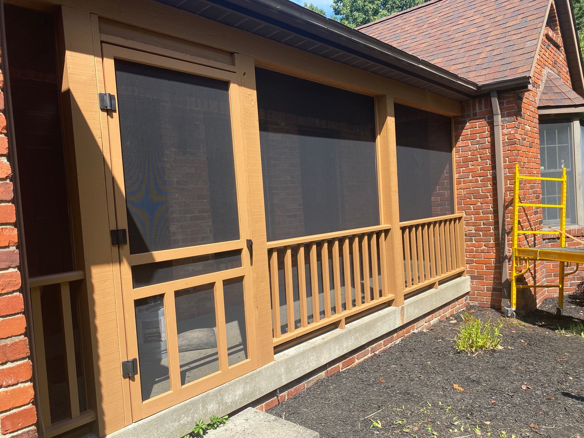 A screened in porch on the side of a brick house