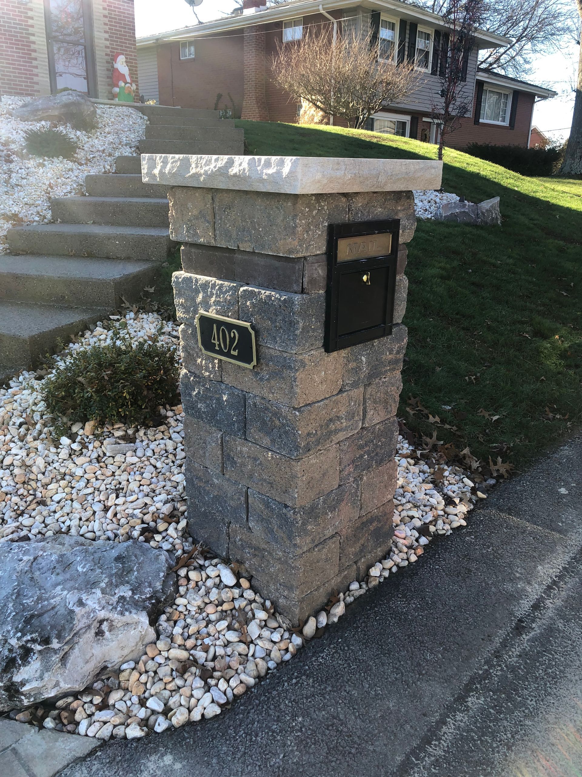 A mailbox is sitting on top of a brick pillar in front of a house.