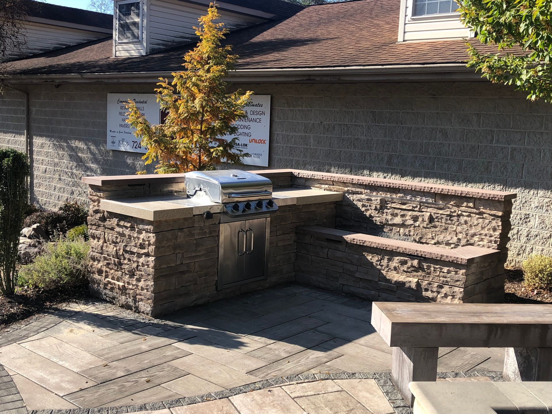 A patio with a grill and a bench in front of a house