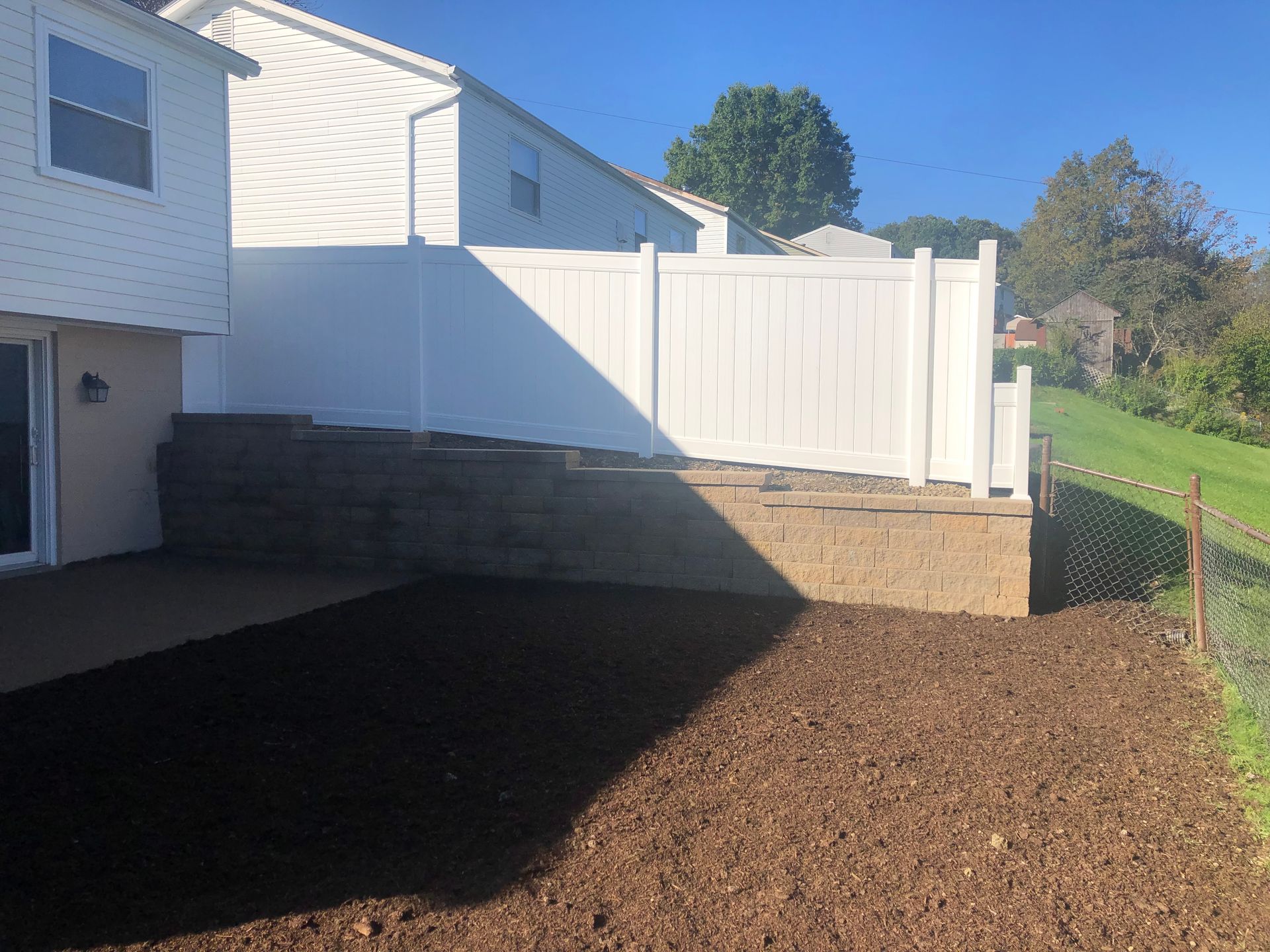 A backyard with a white fence and a brick wall.