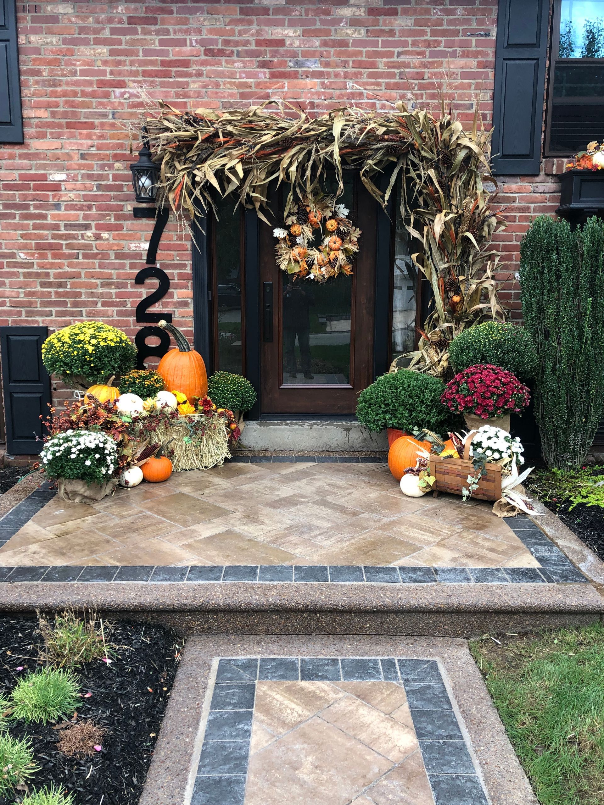 A brick house with a porch decorated for fall with pumpkins and flowers.
