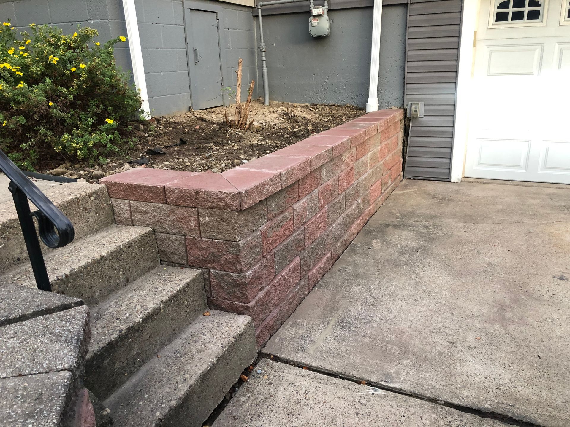 There is a brick wall between the stairs and the garage door.