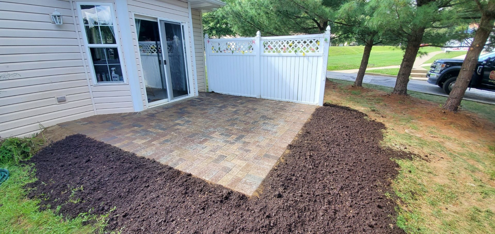 A patio with a white fence and a pile of mulch in front of a house.