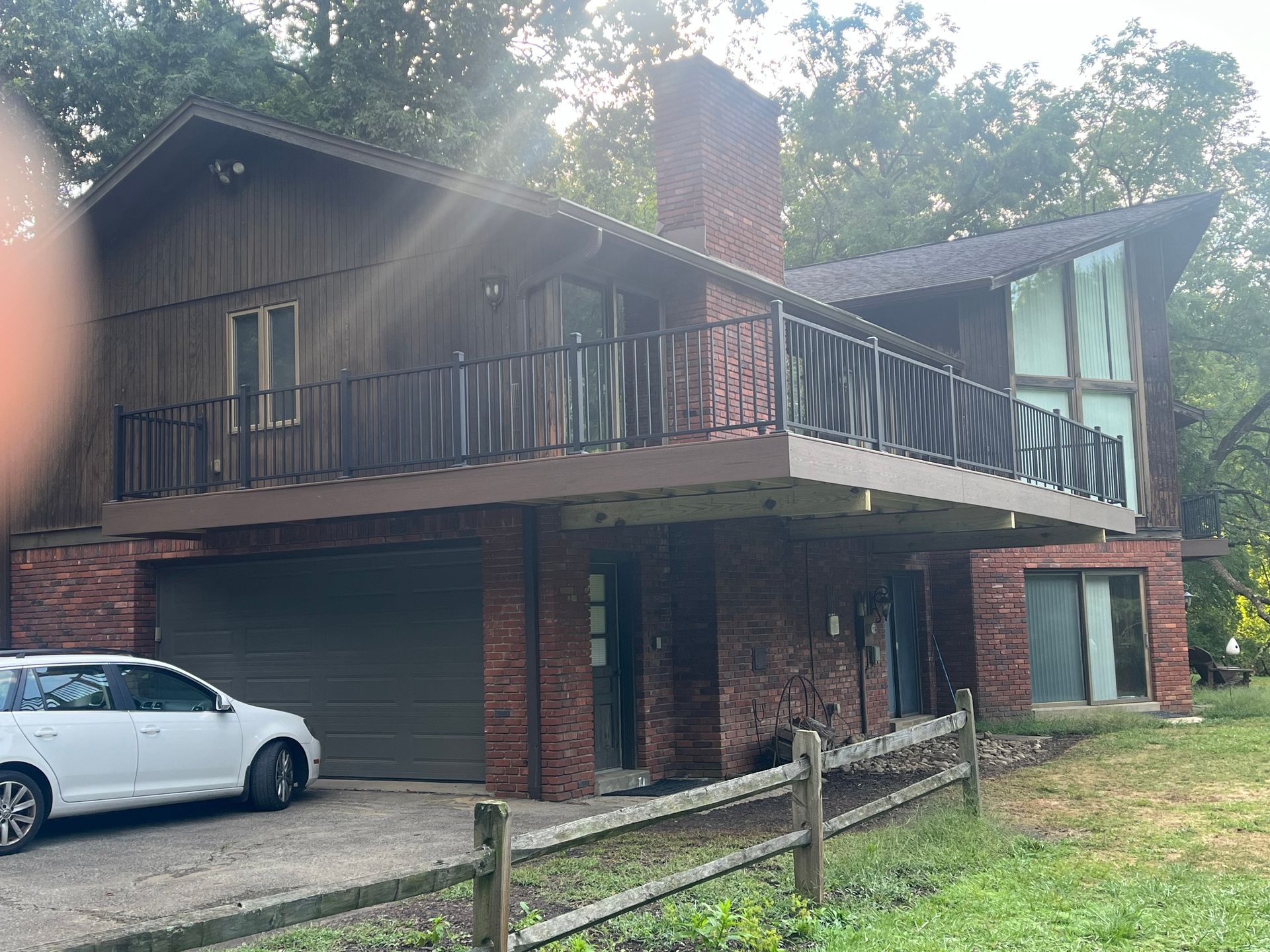 A white car is parked in front of a large house with a balcony.
