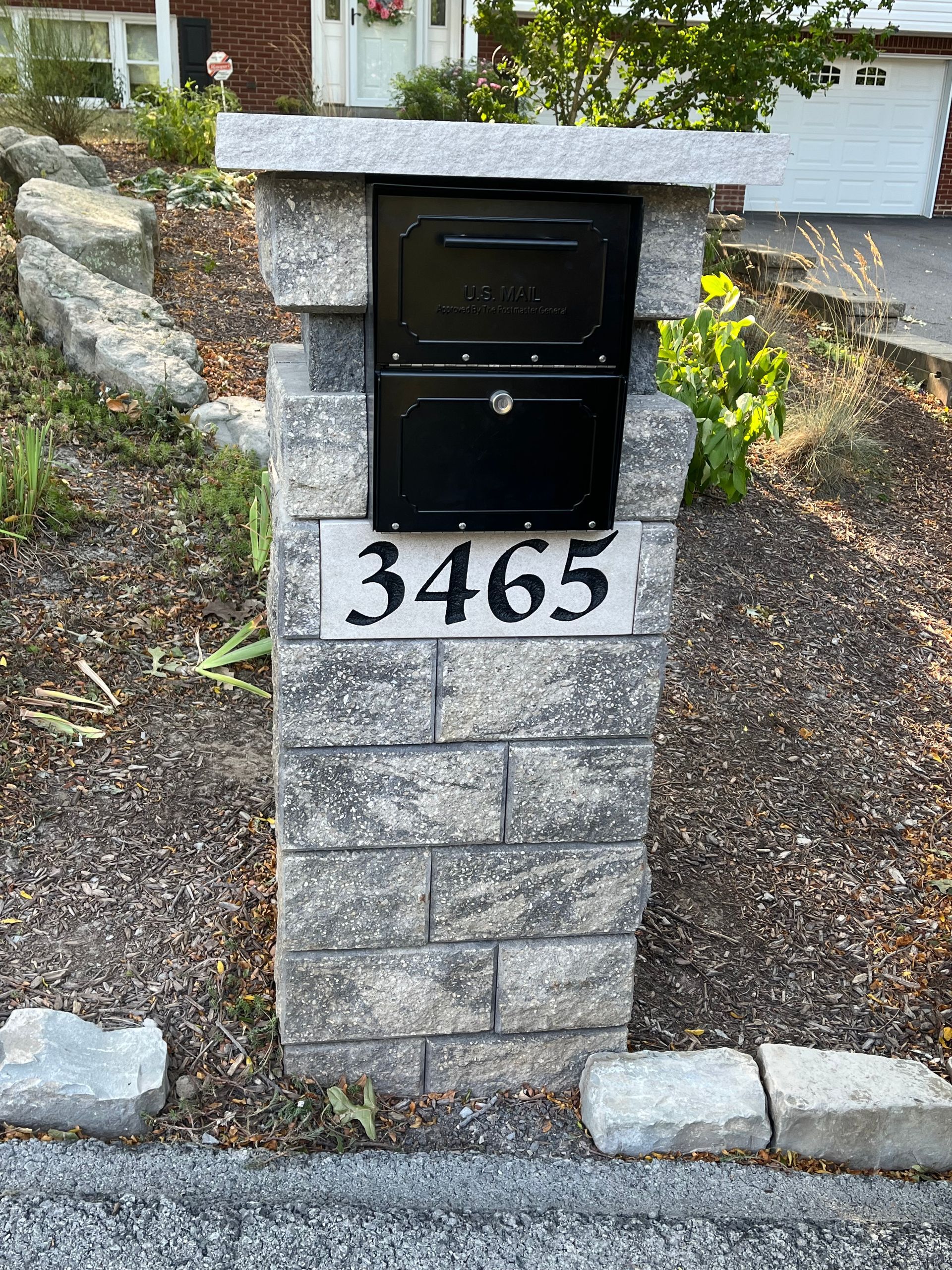 A black mailbox is sitting on top of a brick pillar.